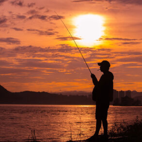 Silhouette of fisherman on lakeshore at sunset
