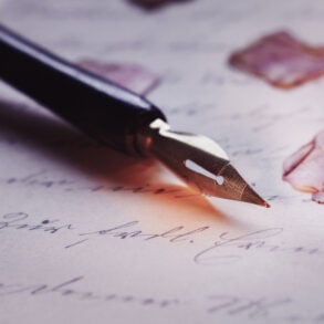 Old-fashioned pen on paper with flower petals