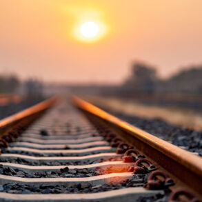 Train tracks under an orange sky with sun