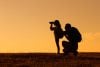 Silhouette of father and daughter with backpacks as daughter looks through binoculars