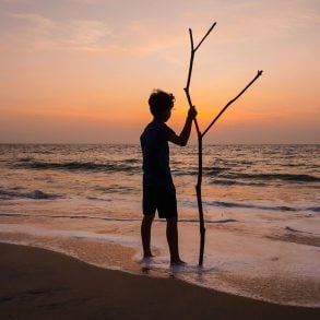 Silhouette of boy with stick on beach of Indian Ocean